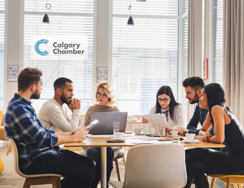 Image of a diverse team of professionals collaboratively working at a large desk, engaged in a brainstorming session. The setting includes laptops, notepads, and digital devices scattered around, with team members actively discussing and sharing ideas. The atmosphere is lively and focused, highlighting effective teamwork and communication in a modern office environment.