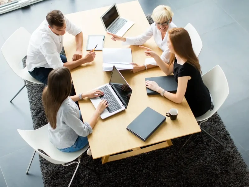 Aerial view of business professionals collaborating at a table, each using laptops for a productive meeting.