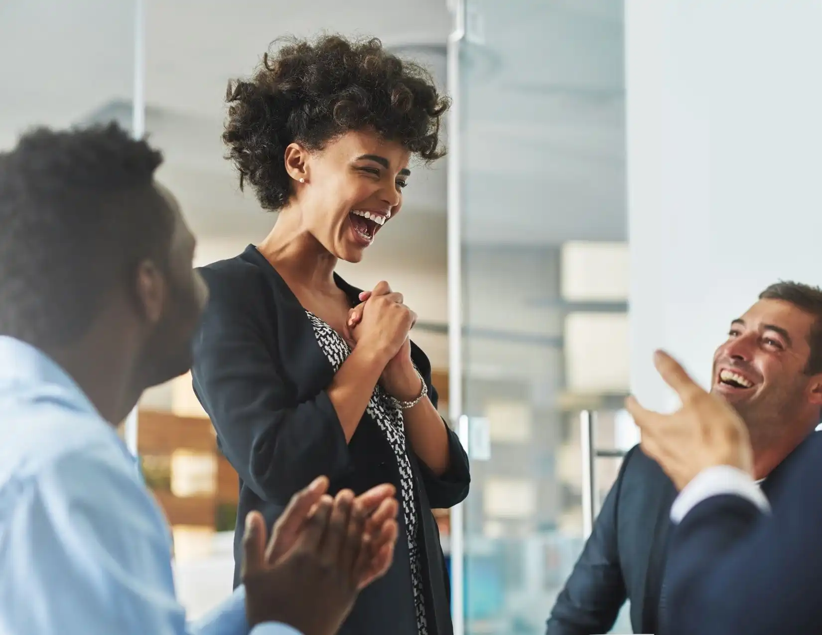 A woman joyfully claps and laughs with her colleagues, celebrating a moment of camaraderie in a professional setting.