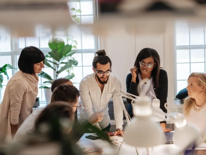 A group of colleagues in an office space, actively participating in a meeting and sharing ideas in a collaborative atmosphere.