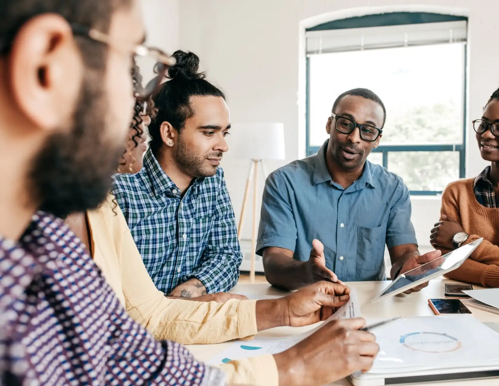 A diverse group of individuals engaged in discussion around a table, with a tablet open in front of them.