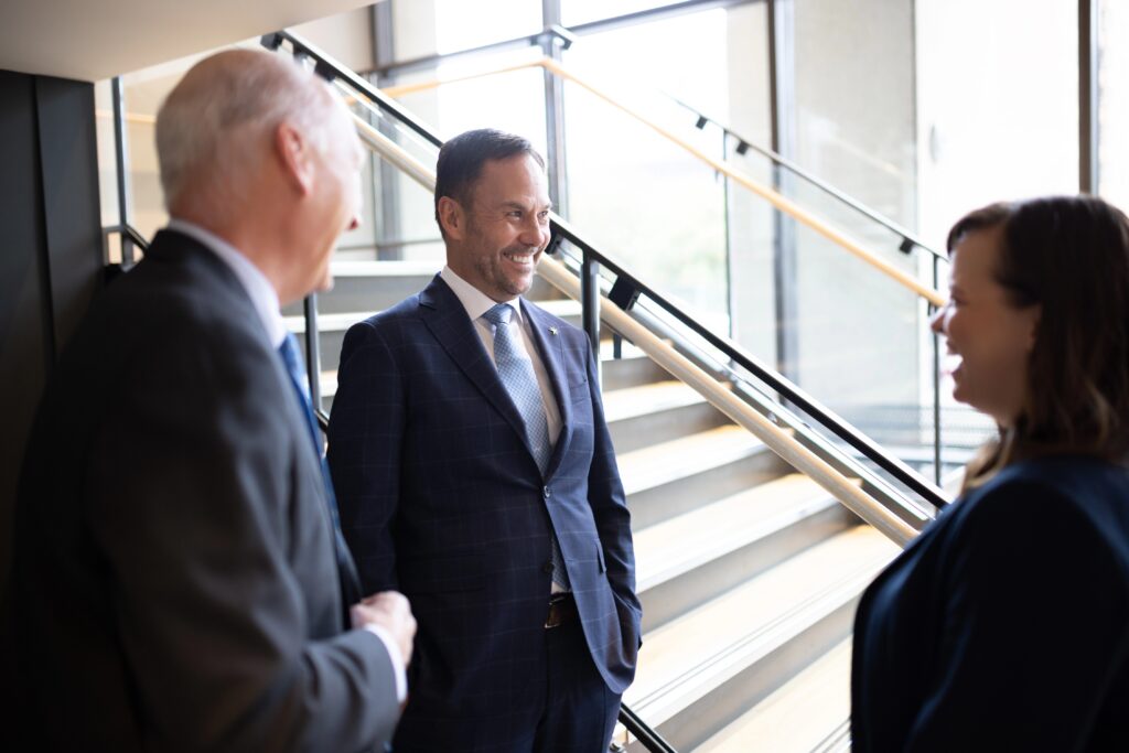 Three Bright Wire Leadership coaches and consultants engaged in a discussion by a modern staircase, exemplifying humility in leadership.