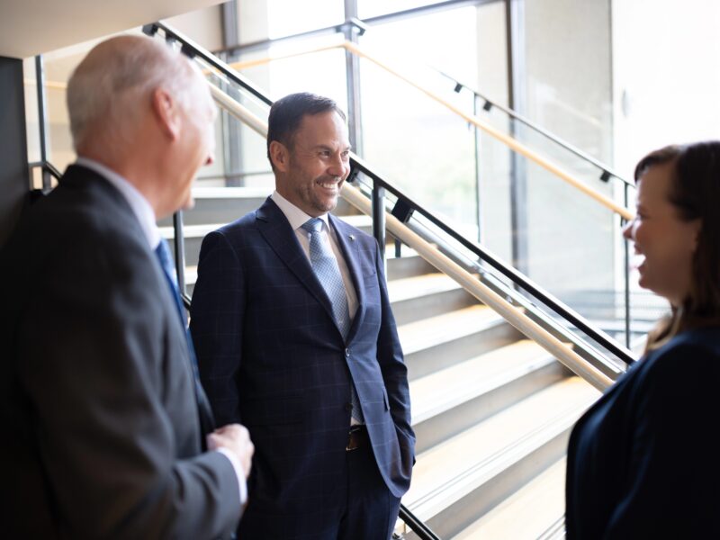 Three Bright Wire Leadership coaches and consultants engaged in a discussion by a modern staircase, exemplifying humility in leadership.